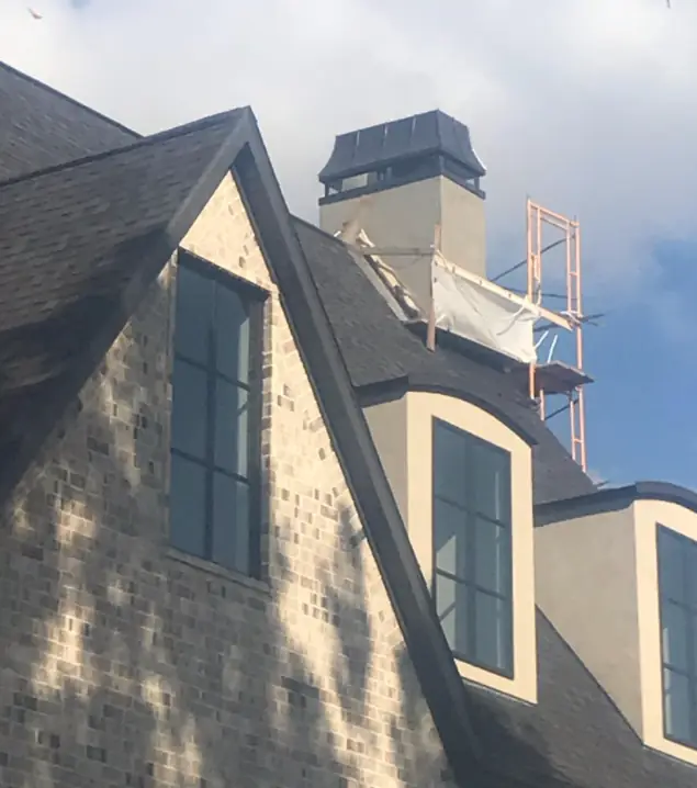 Brick and stucco home with steep dark-shingle gables and dormers during exterior work
