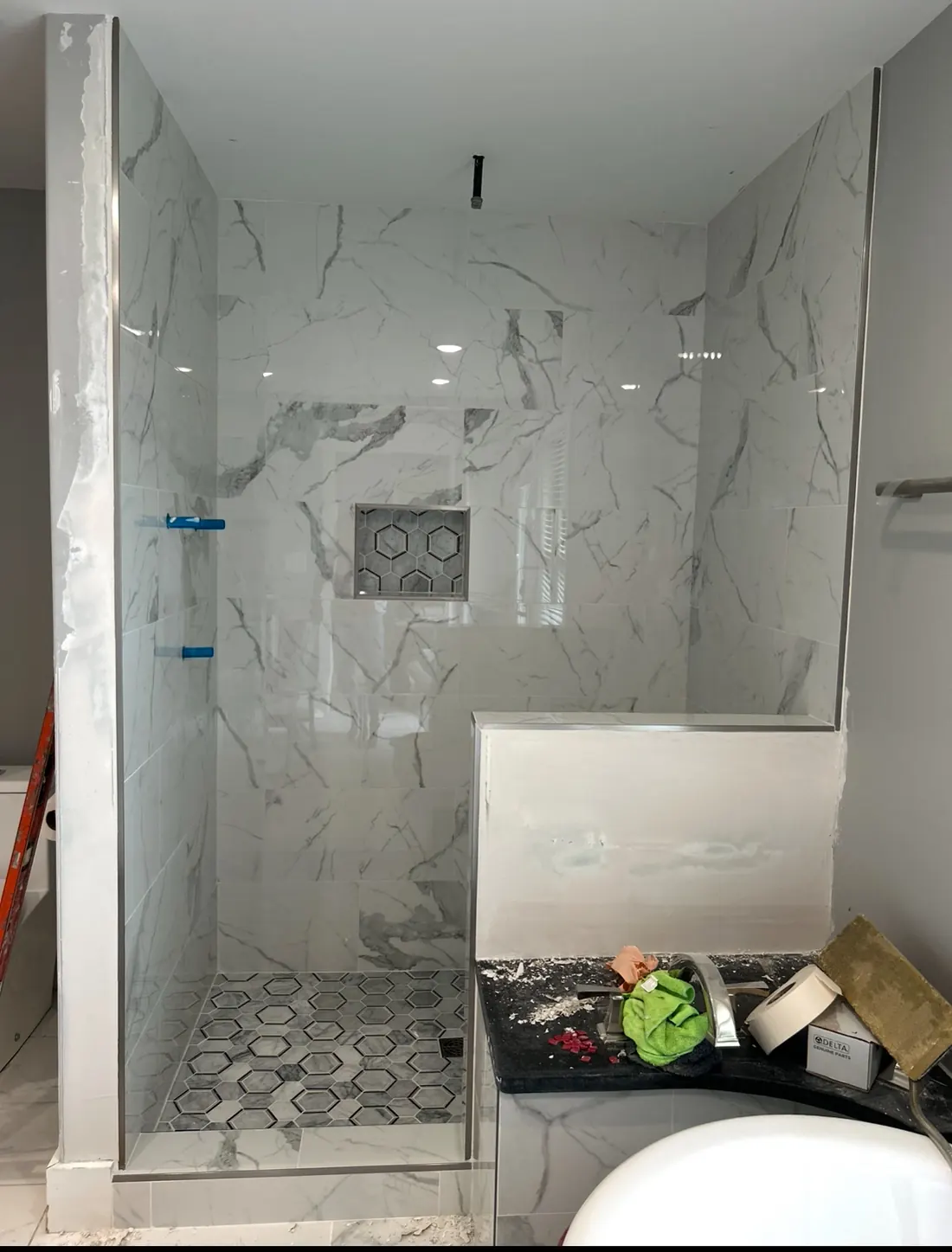 Finished walk-in shower by JMI with veined porcelain slabs, frameless glass and a hex mosaic floor